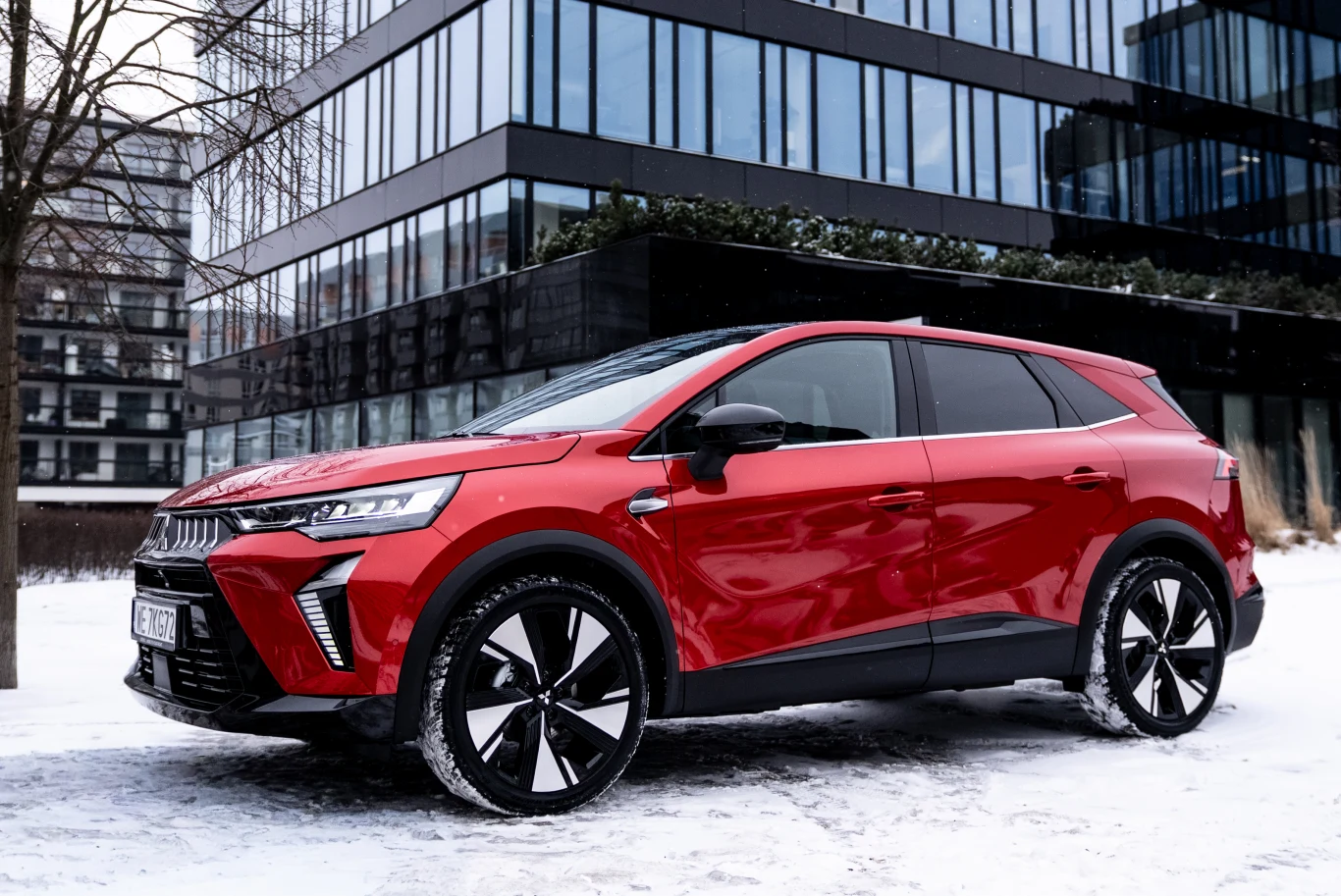 Czerwony SUV o nowoczesnym, dynamicznym designie stoi na śniegu przed szklanym biurowcem, wyraźnie kontrastując z zimowym otoczeniem dzięki efektownym czarno-srebrnym felgom i agresywnej linii nadwozia.