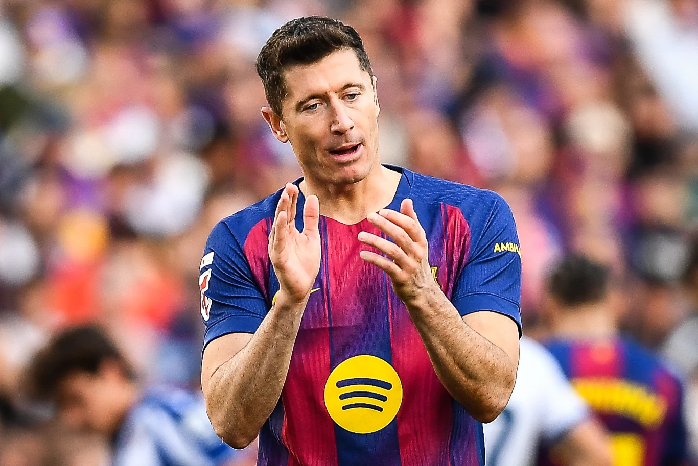 Robert Lewandowski Robert Lewandowski w koszulce FC Barcelona z logotypem Spotify klaska na tle stadionu i piłkarzy.