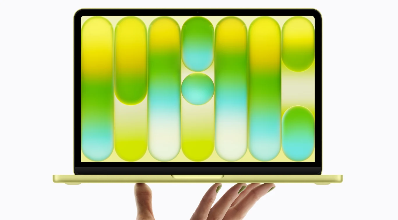 Smukły, żółty laptop trzymany na dłoni, z wyświetlaczem prezentującym kolorową grafikę w odcieniach żółci, zieleni i błękitu z geometrycznymi kształtami.