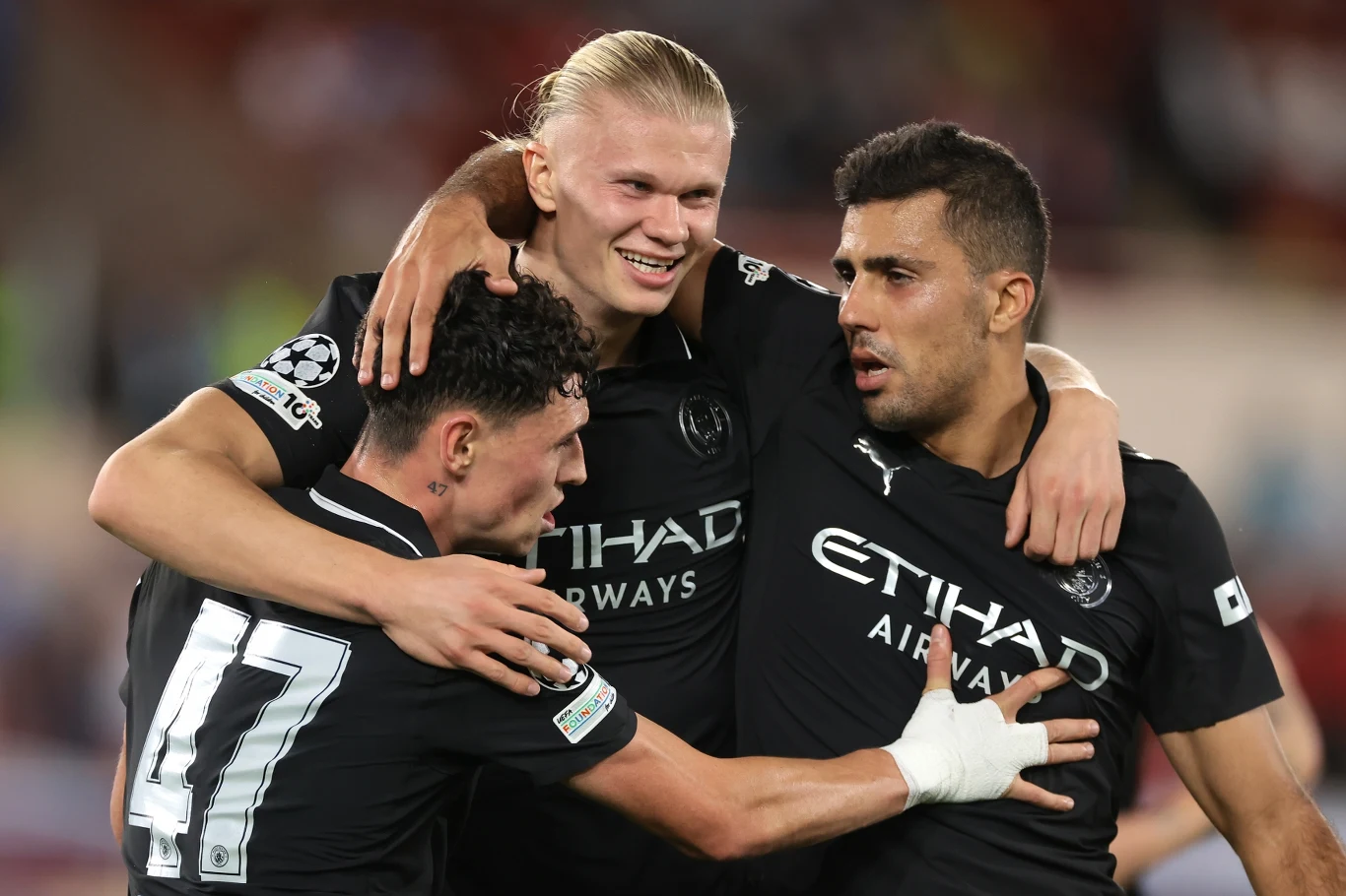 Erling Haaland, Phil Foden i Rodri w czarnych strojach Manchester City świętują gola, obejmując się na boisku.