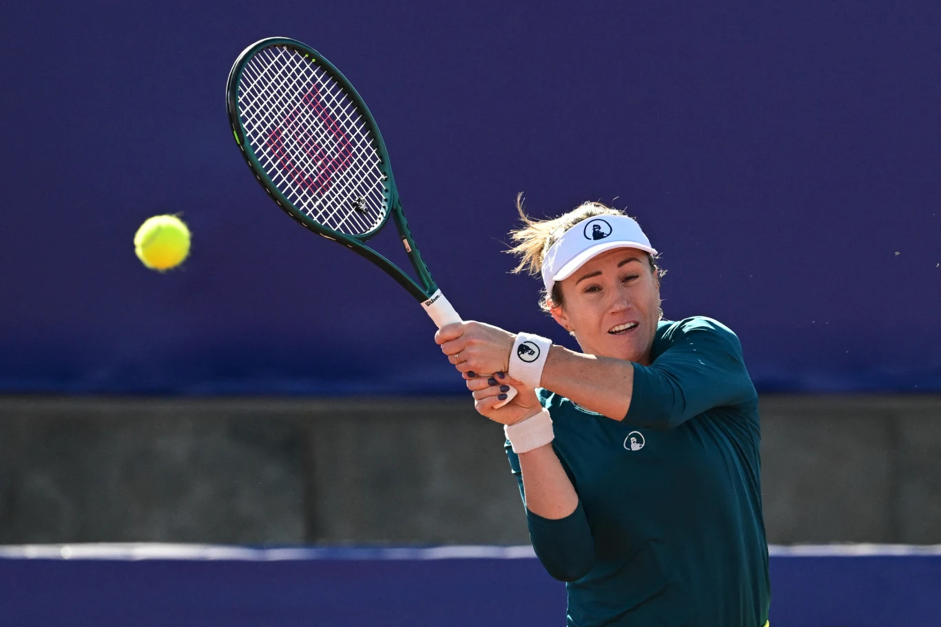 Un jugador de tenis con un traje verde durante un golpe dinámico de revés a dos manos, una pelota de tenis que se acerca contra el fondo de una cancha azul.