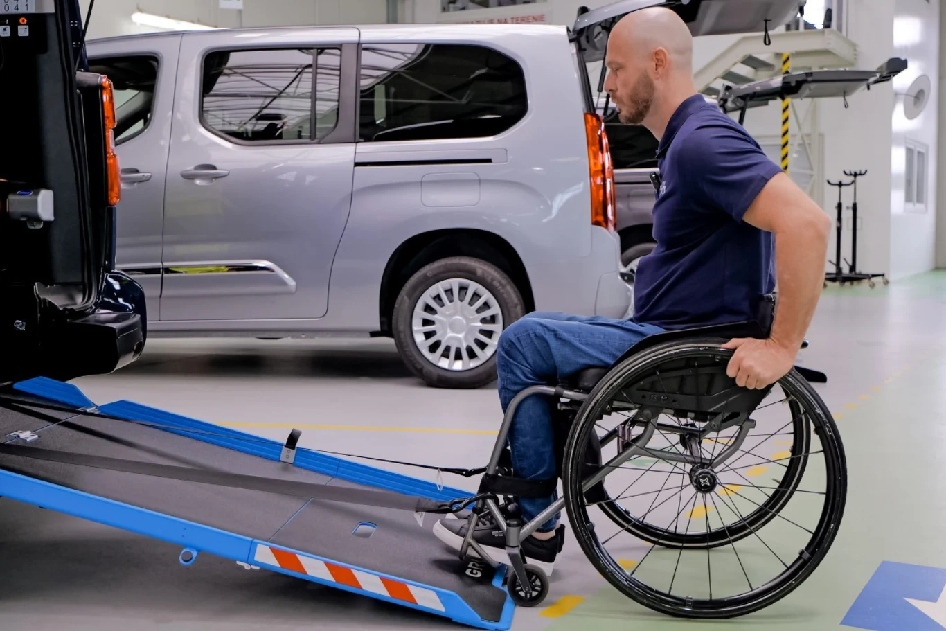 PFRON pokrywa nawet do 85 proc. wartości nowego auta. Mężczyzna na wózku inwalidzkim podjeżdżający rampą do wnętrza specjalnie przystosowanego pojazdu, w tle jasny samochód dostawczy zaparkowany w hali.
