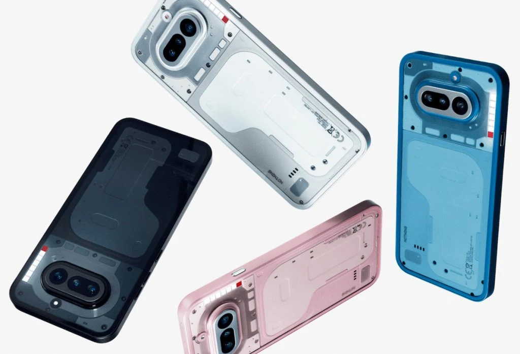 Smartfon Nothing Phone 4a. Cztery smartfony w różnych kolorach — czarnym, białym, różowym i niebieskim — unoszą się na jasnym tle, każdy z przezroczystą lub półprzezroczystą obudową ukazującą elementy konstrukcyjne i podwójny aparat z zaokrąglonymi rogami.