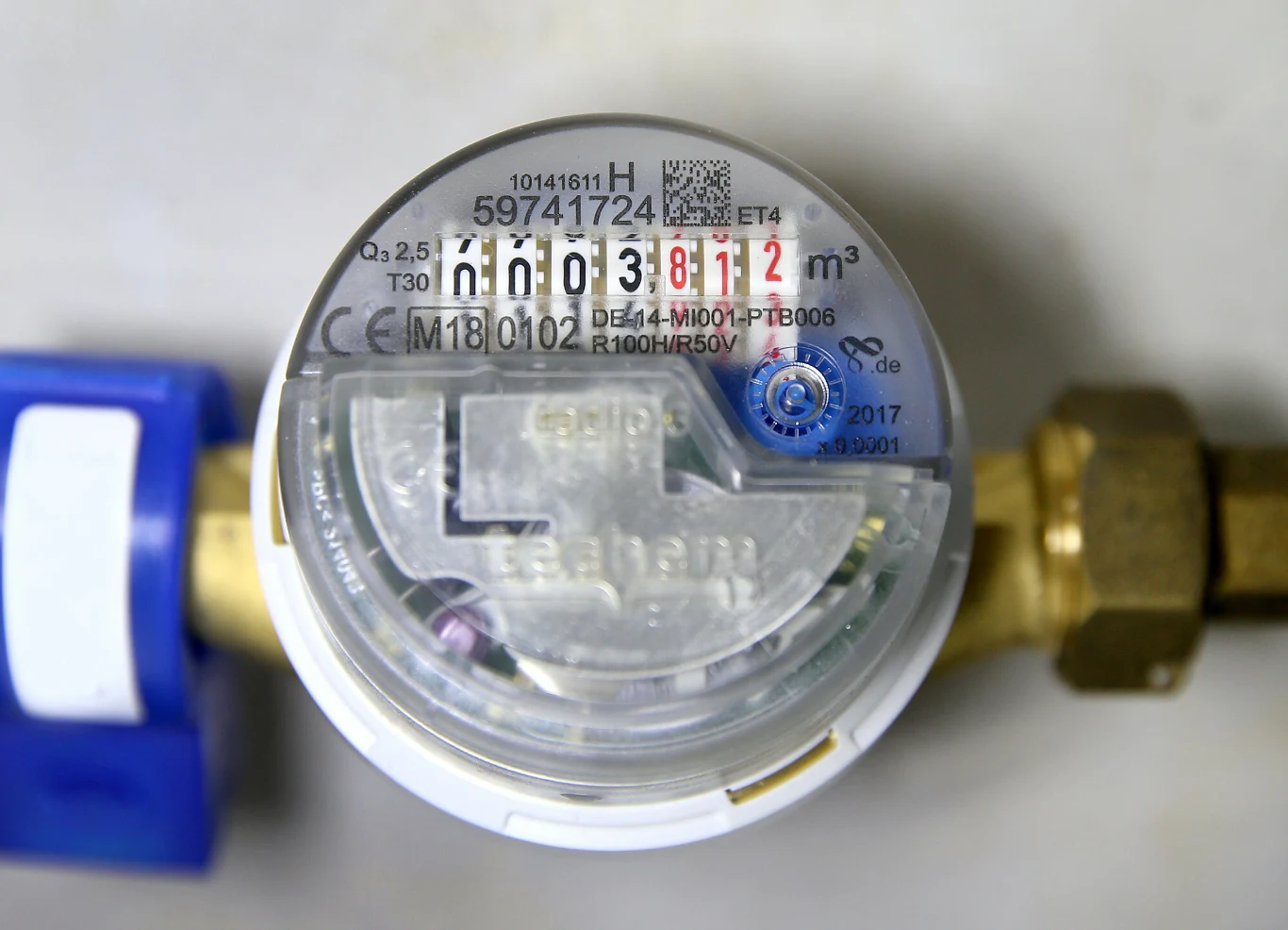 Wodomierze do wymiany Licznik wody z czytelnym wskazaniem zużycia, cyfrowym liczydłem oraz plastikową osłoną, podłączony do instalacji wodnej za pomocą metalowych złączek i niebieskiego zaworu po lewej stronie.