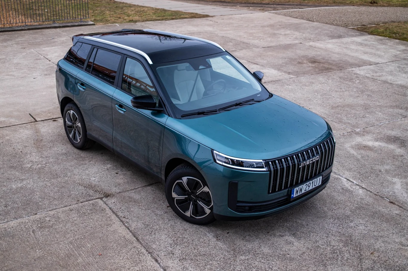 Nowoczesny, zielony SUV o dynamicznej sylwetce z charakterystycznym przodem wyposażonym w pionowe chromowane listwy na grillu, czarny dach z panoramicznym oknem oraz aerodynamiczne felgi.