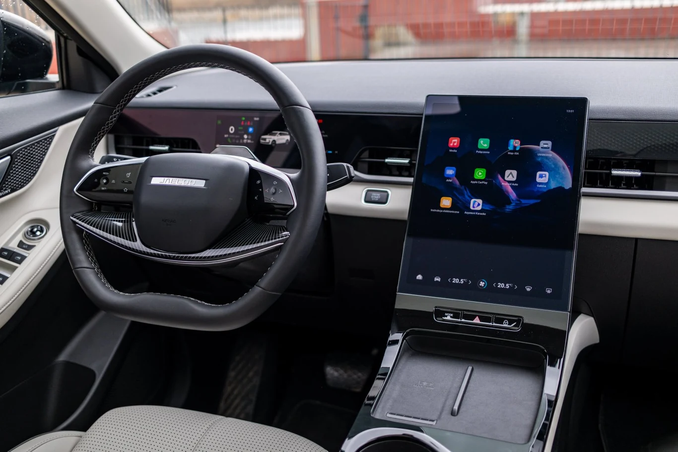 Nowoczesne wnętrze samochodu z cyfrowym wyświetlaczem na desce rozdzielczej i dużym, pionowym ekranem dotykowym na konsoli centralnej, otoczone minimalistycznym designem oraz jasną tapicerką fotela kierowcy.