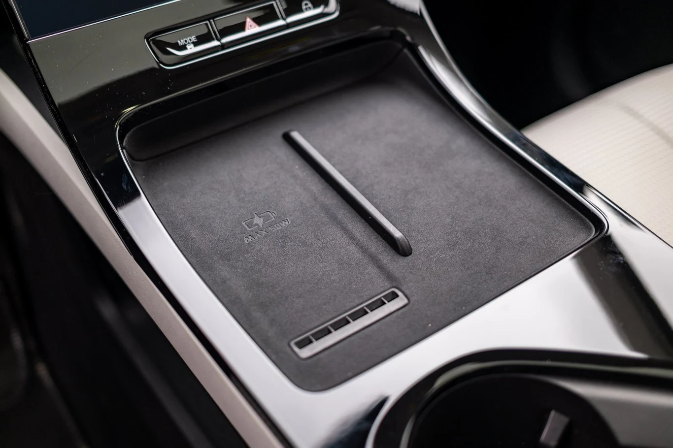 Panel centralny samochodu z bezprzewodową ładowarką do smartfonów, otoczony czarnym i chromowanym wykończeniem, obok znajduje się część uchwytu na napoje.