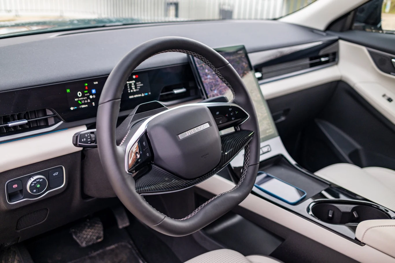 Nowoczesna deska rozdzielcza z cyfrowymi wyświetlaczami, wielofunkcyjna kierownica oraz duży pionowy ekran dotykowy centralny, całość utrzymana w minimalistycznym stylu z jasną tapicerką i czarnymi detalami.