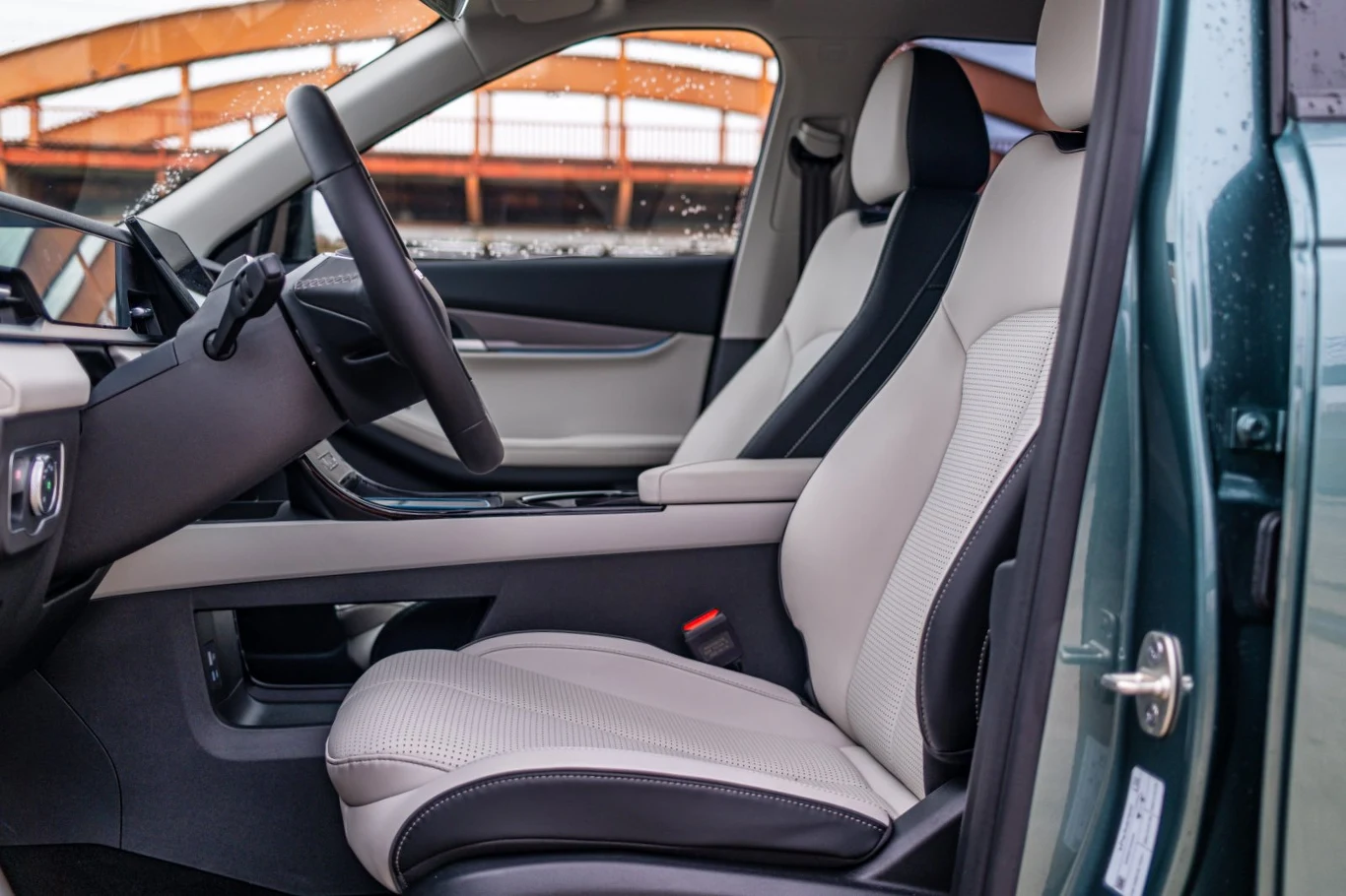 Wnętrze samochodu z jasną, skórzaną tapicerką foteli, czarną deską rozdzielczą, wielofunkcyjną kierownicą i widocznym pasem bezpieczeństwa po stronie pasażera.