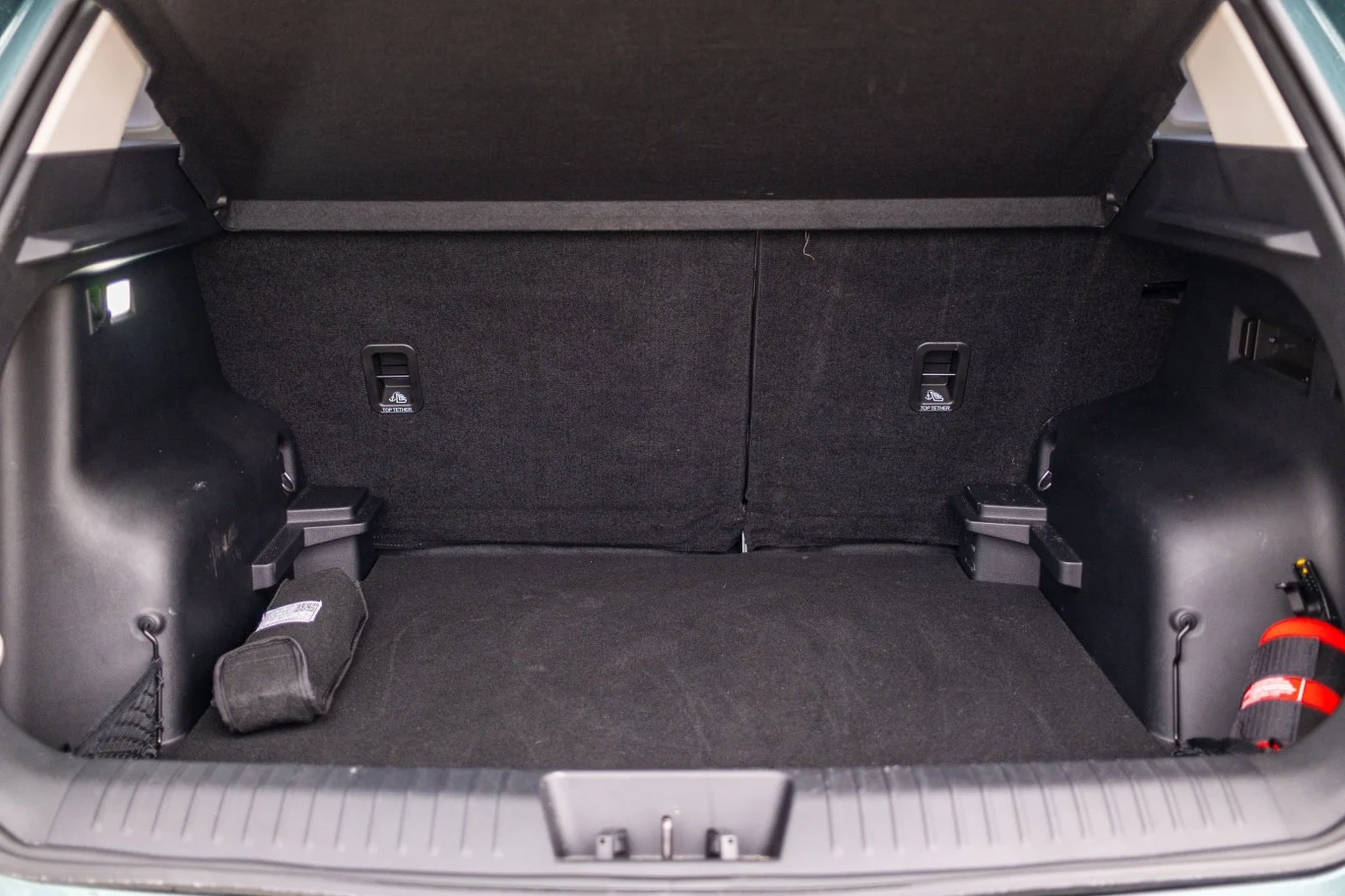 Pojemny, czysty bagażnik samochodu z widocznymi zaczepami do mocowania ładunku, osłoniętą gaśnicą po prawej stronie oraz schowkiem na lewym nadkolu.