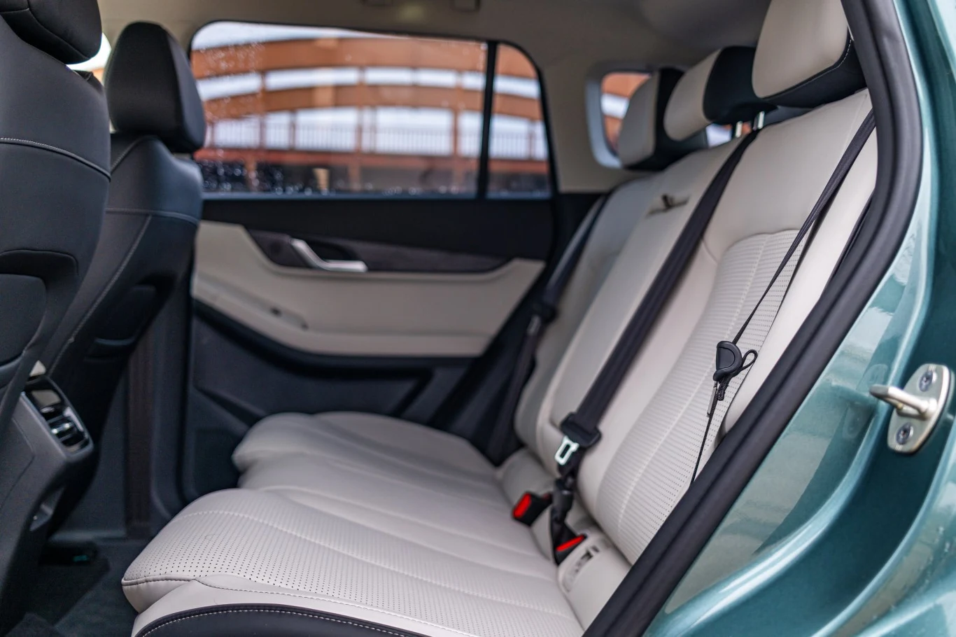 Jasna, skórzana tapicerka na tylnych siedzeniach samochodu osobowego, z wyraźnie widocznymi pasami bezpieczeństwa i minimalistycznym wykończeniem drzwi.