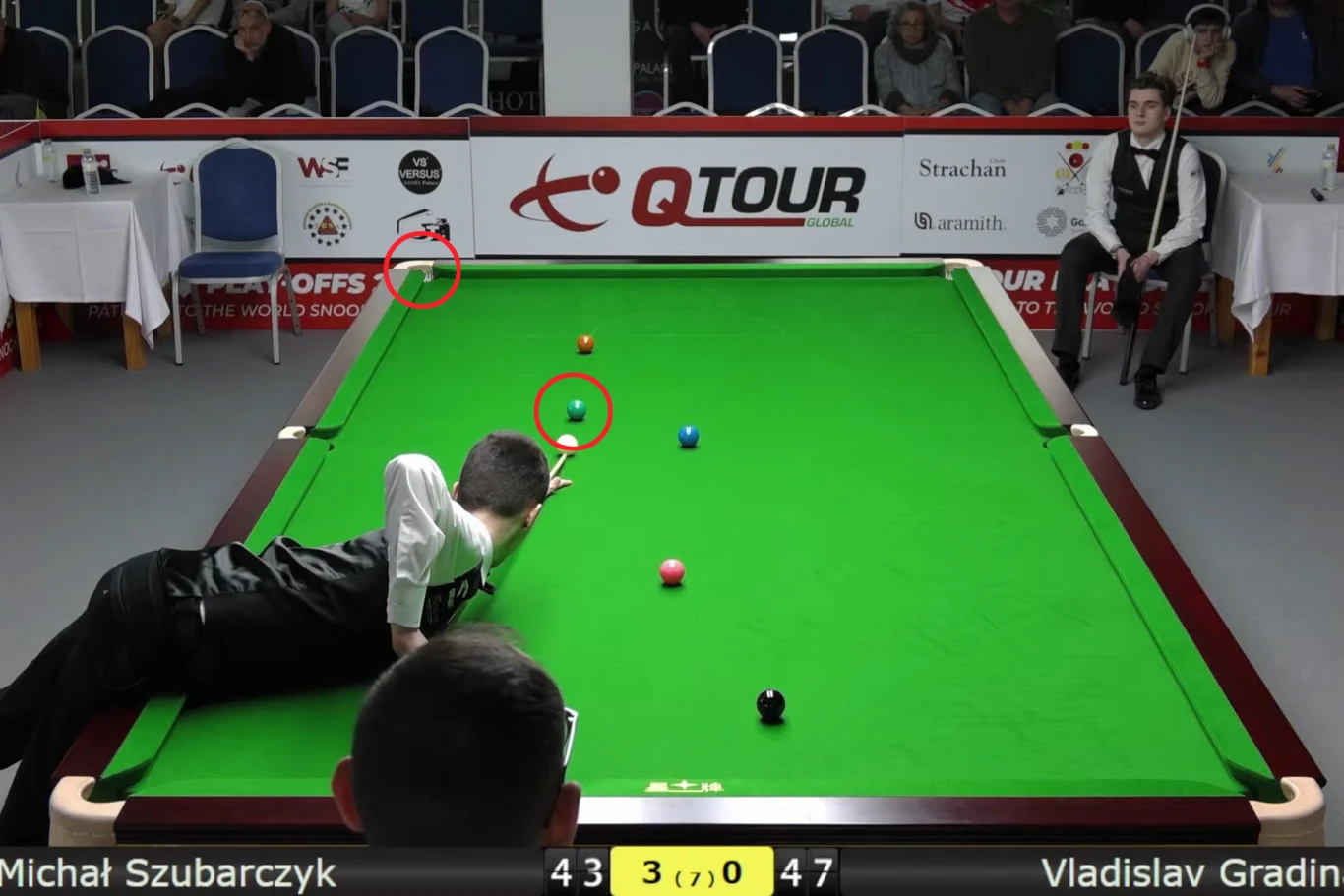 Zawodnik wykonuje precyzyjne uderzenie bilą białą na zielonym stole snookerowym, w tle siedzą sędzia oraz widzowie, a na bandzie widoczne są logotypy sponsorów turnieju Q Tour.