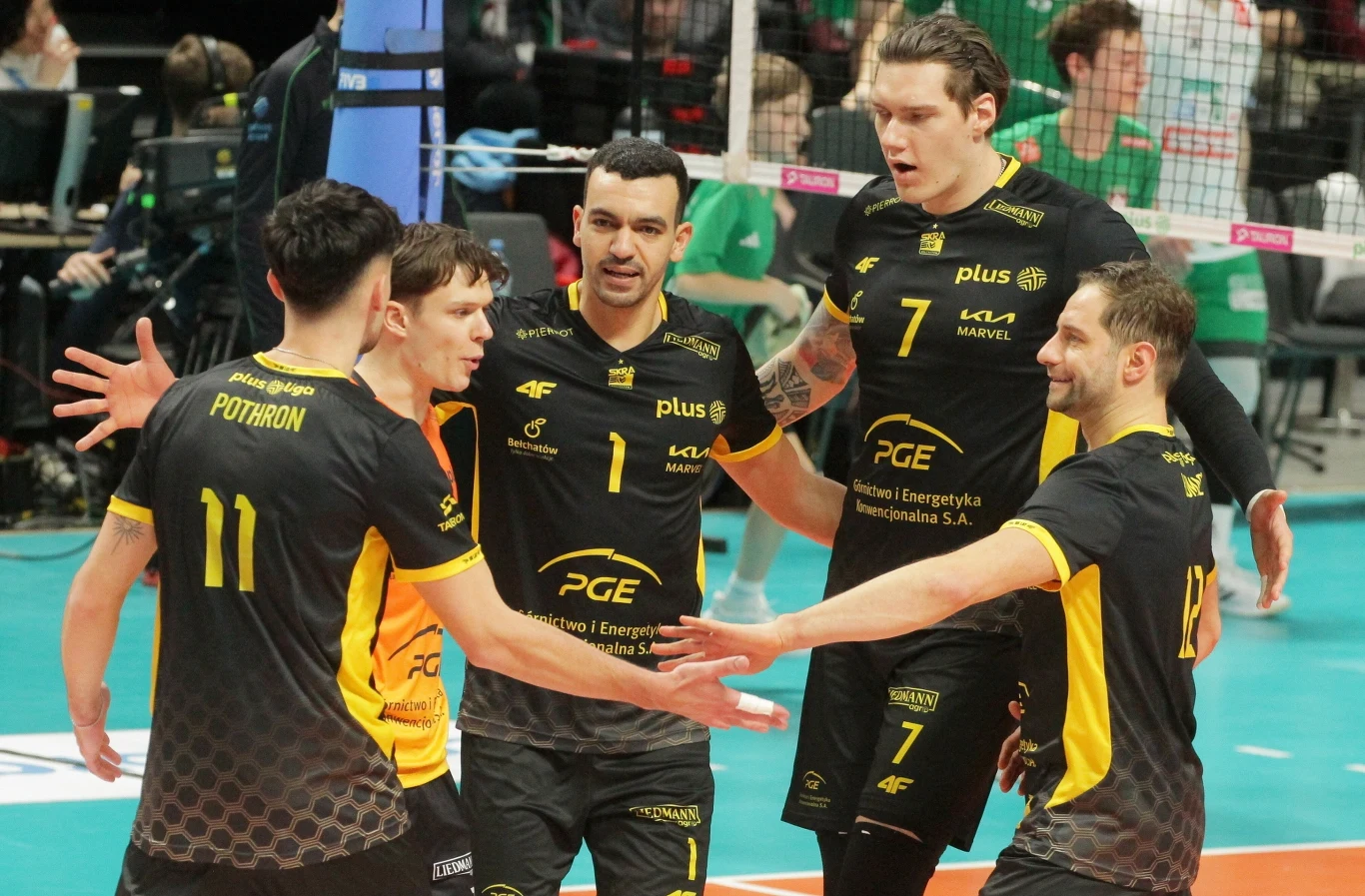 Siatkarze drużyny PGE Skra Bełchatów w czarnych i żółtych strojach celebrują zdobycie punktu na boisku, w tle widoczni zawodnicy drużyny przeciwnej w zielonych strojach za siatką.