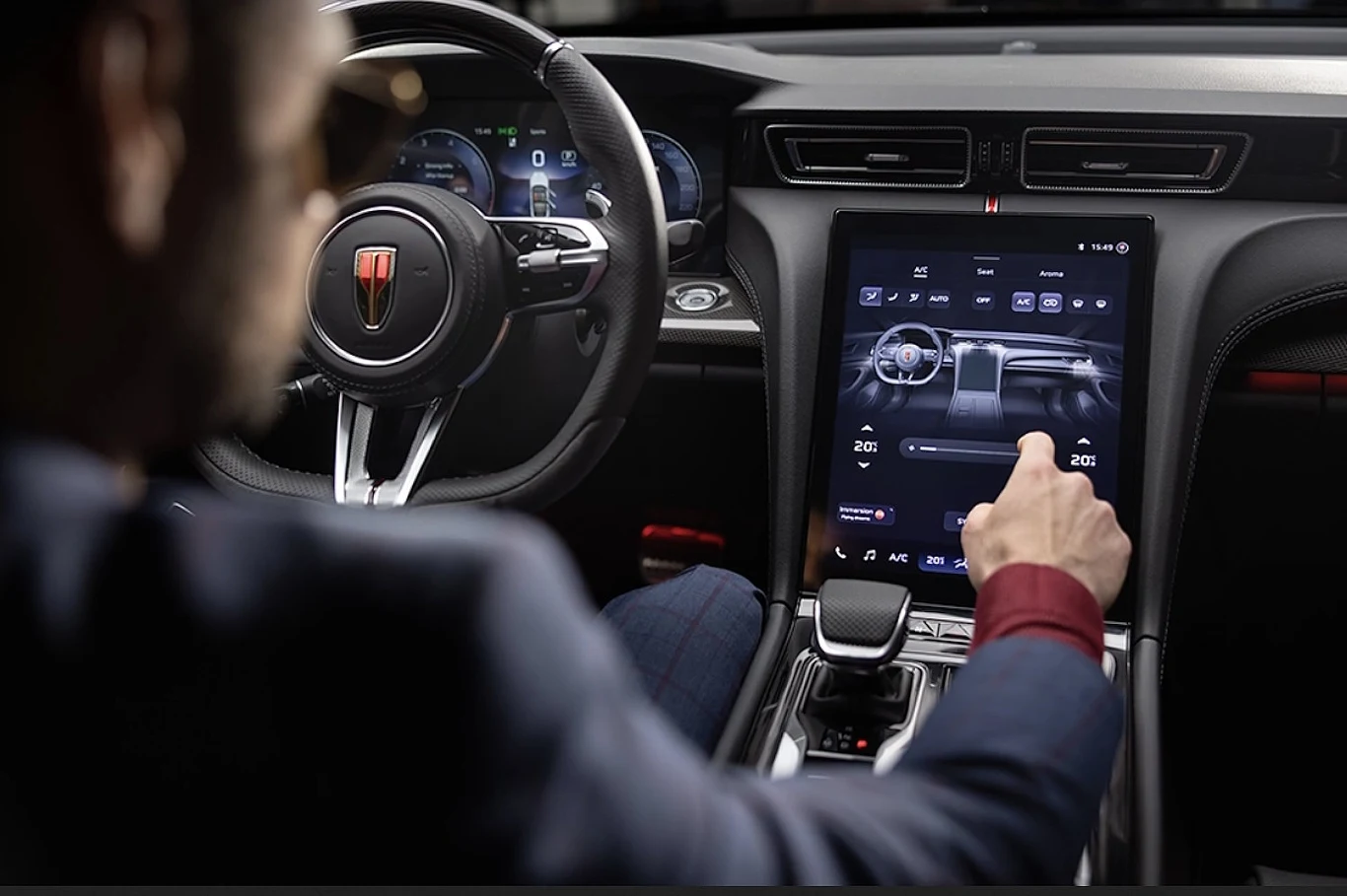 Wnętrze Hongqi H6 Mężczyzna w eleganckim stroju obsługuje duży, nowoczesny ekran dotykowy w luksusowym wnętrzu samochodu, z widoczną cyfrową deską rozdzielczą oraz logo marki na kierownicy.