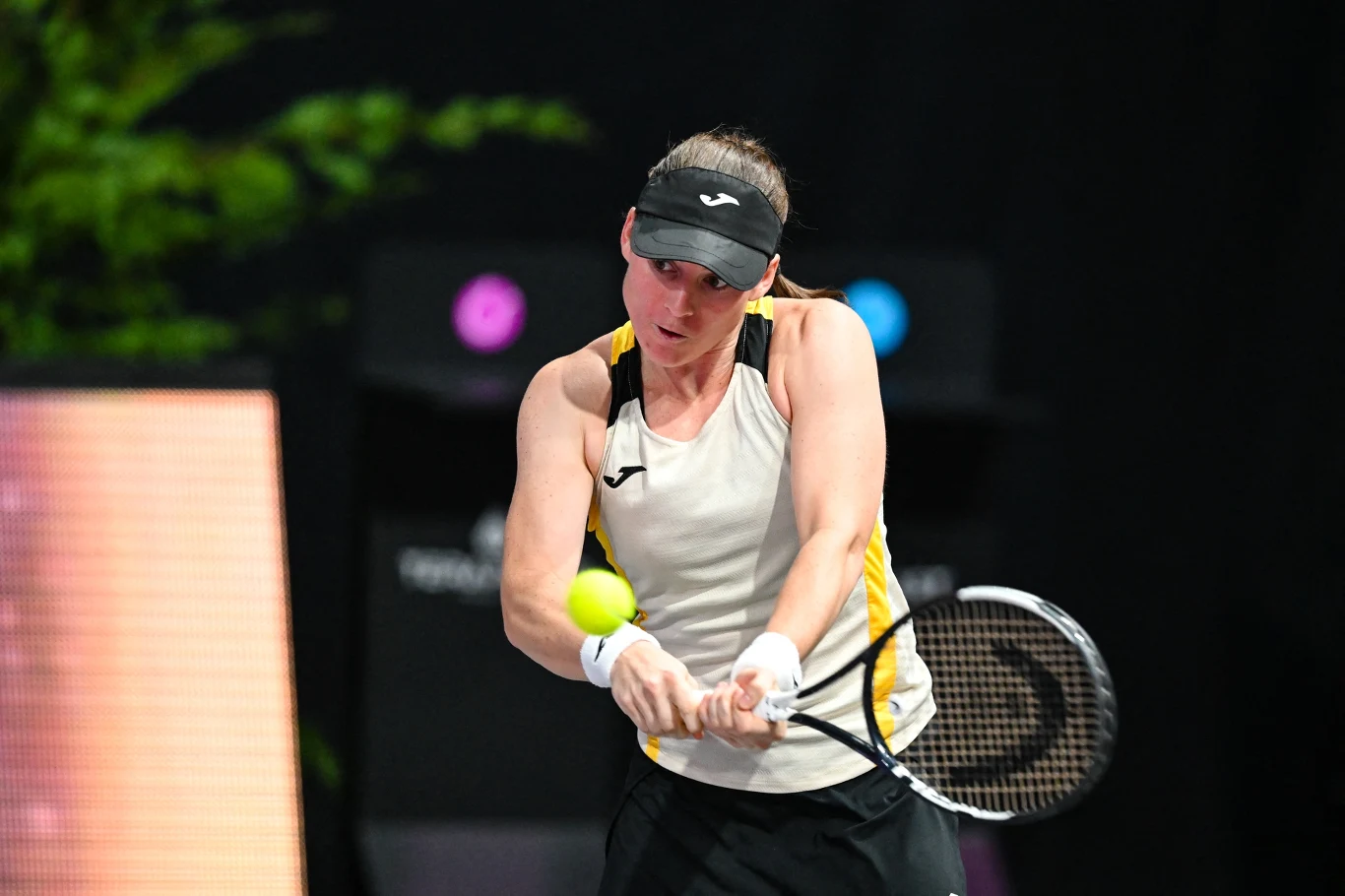 Tenisistka w sportowym stroju uderza piłkę rakietą w trakcie meczu, koncentrując się na precyzyjnym wykonaniu uderzenia na tle zamazanego kortu.