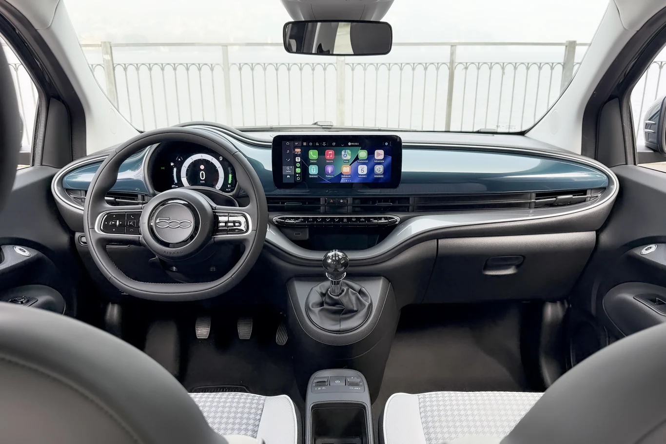 Nowoczesna deska rozdzielcza z cyfrowym zestawem wskaźników, centralnym ekranem dotykowym z funkcją Android Auto, wielofunkcyjną kierownicą oraz manualną dźwignią zmiany biegów, wykończenie wnętrza w jasnych i ciemnych odcieniach.