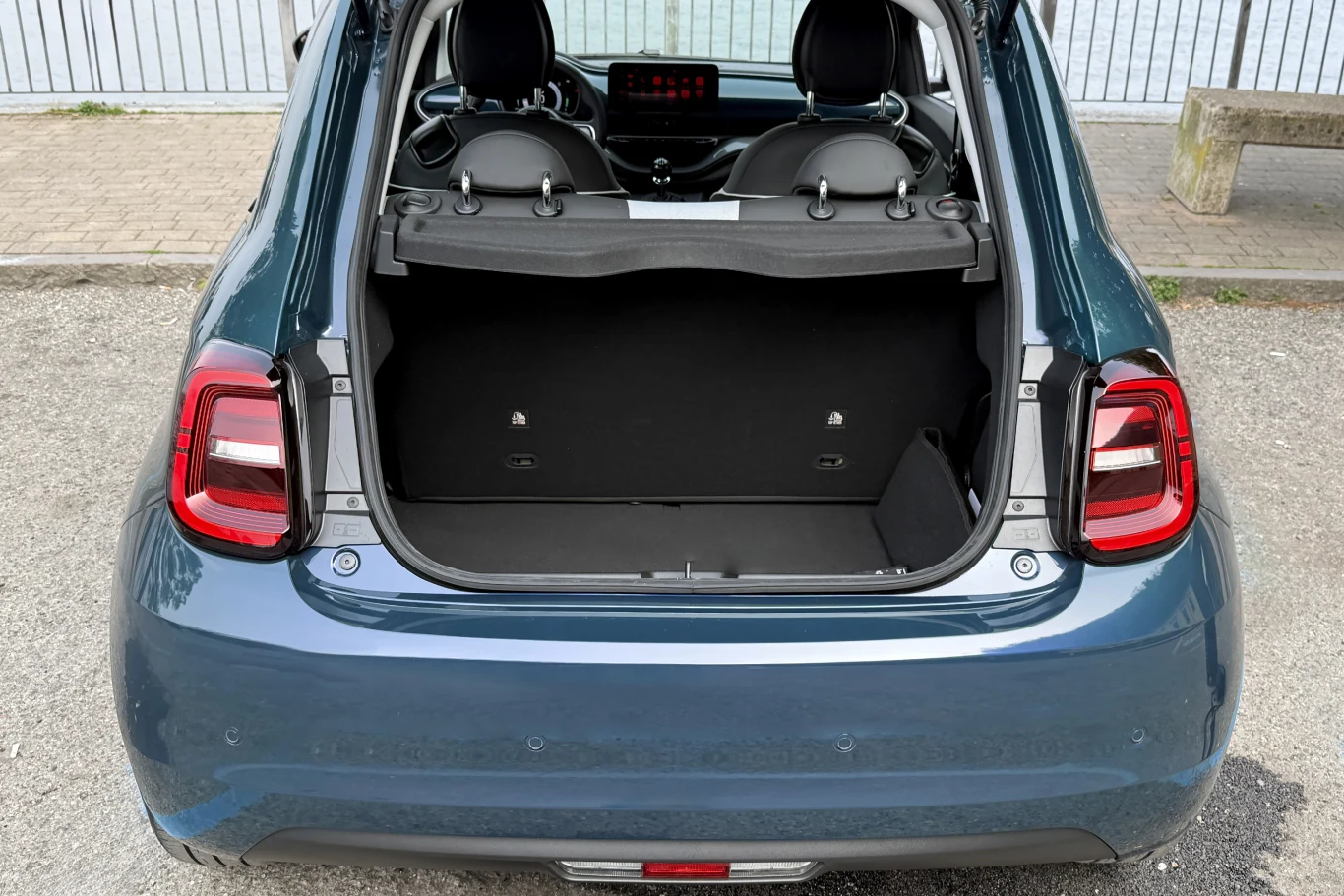 Otwarty bagażnik niebieskiego samochodu miejskiego, widoczne tylne światła LED, dwa przednie fotele oraz ekran wewnątrz pojazdu.