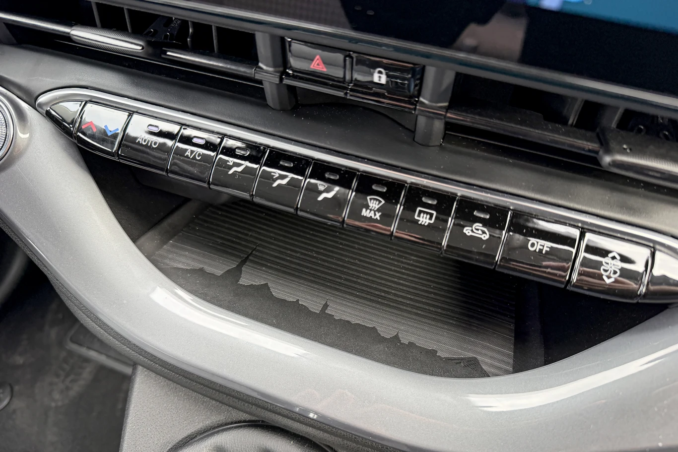 Panel sterowania klimatyzacją w samochodzie z szeregiem przycisków funkcyjnych, w tym przyciskami do regulacji nawiewu, ogrzewania, klimatyzacji oraz obiegu powietrza, umieszczony poniżej ekranu multimedialnego.