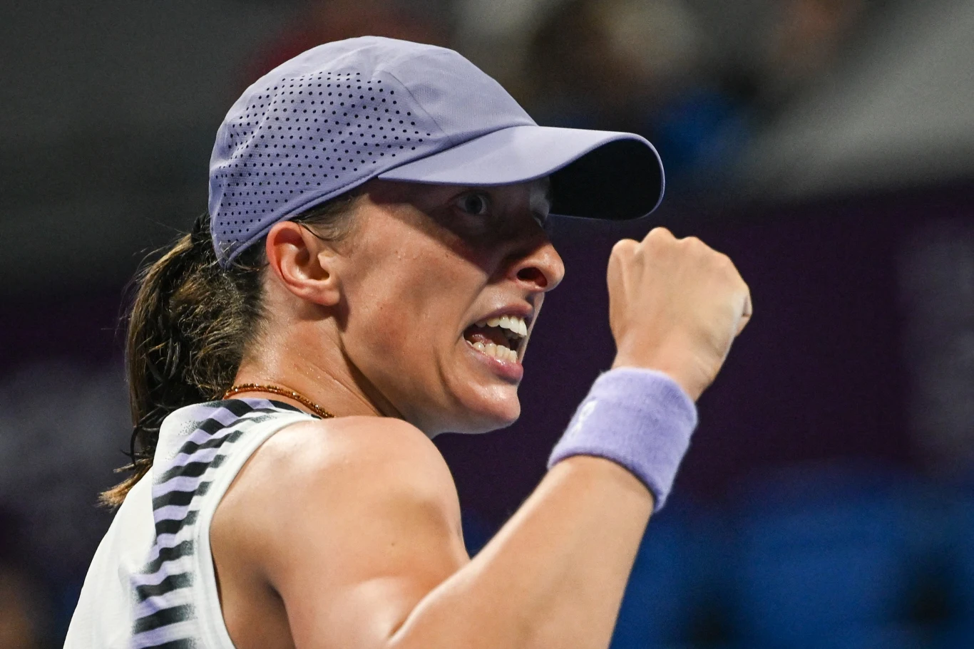 Kobieta w sportowej czapce i opasce na nadgarstku z zaciśniętą pięścią wyraża silne emocje, prawdopodobnie po udanej akcji podczas meczu tenisowego.