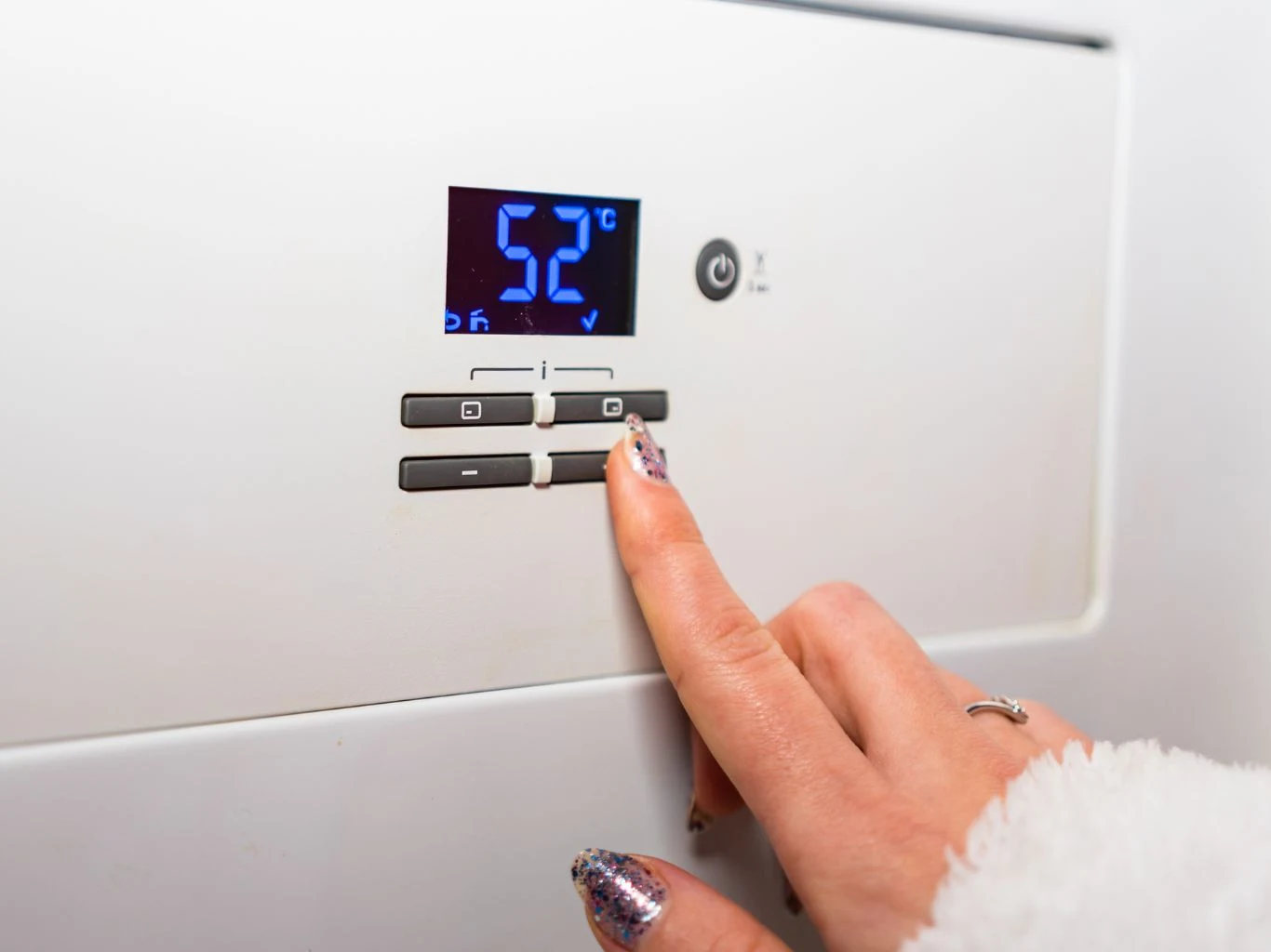 Jednym z najczęściej wykrywanych błędów jest montaż urządzenia, które nie spełnia wymagań programu. Palec naciskający przycisk na panelu sterowania elektronicznego urządzenia z wyświetlaczem pokazującym temperaturę 52°C.