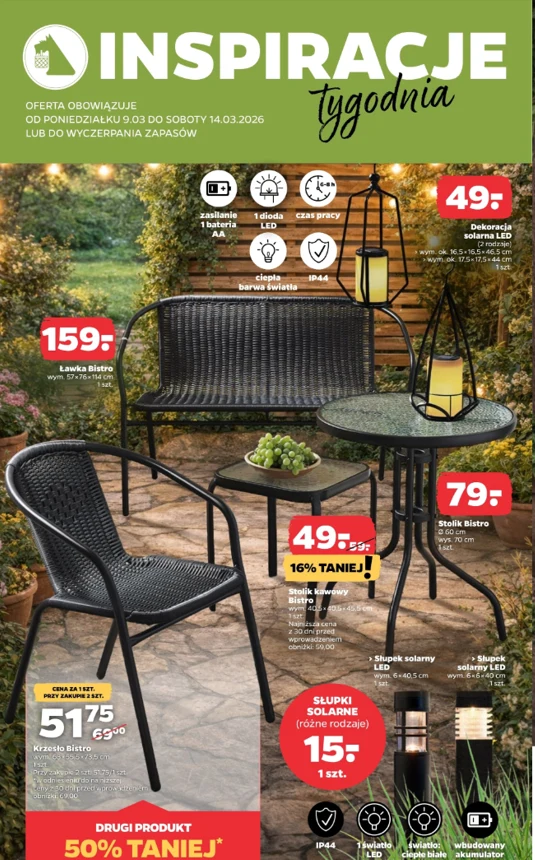 Zestaw ogrodowy składający się z czarnej ławki, dwóch krzeseł i okrągłego stołu z dekoracyjnymi lampionami oraz świecącymi słupkami solarnymi ustawionymi na kamiennej nawierzchni w otoczeniu zieleni.