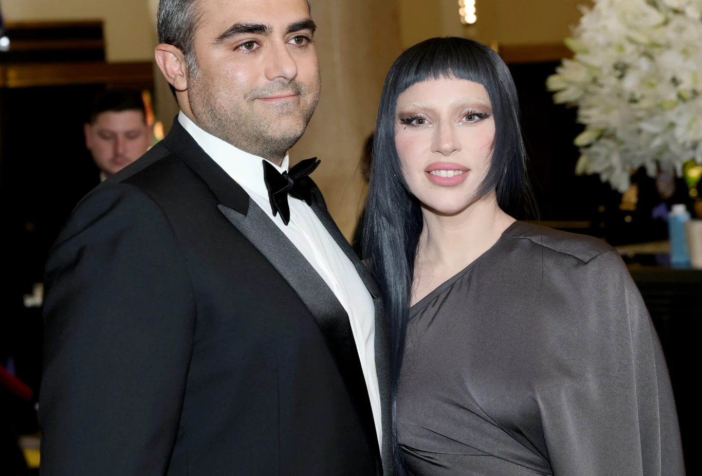 Lady Gaga z narzeczonym Michael Polansky i Lady Gaga pozują do zdjęcia. Mężczyzna jest ubrany w smoking, a kobieta w szarą suknię