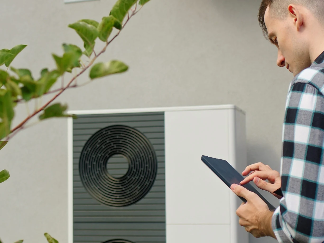 Ruszyły kontrole dotyczące pomp ciepła. Czy masz się czego obawiać? Kontroler z tabletem przy nowoczesnej pompie ciepła zamontowanej na ścianie budynku.
