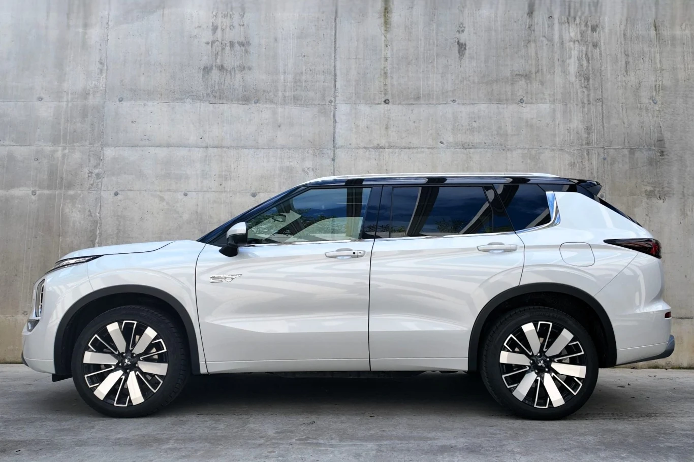 Biały, nowoczesny SUV z ciemnymi szybami i charakterystycznymi, dużymi felgami na tle szarej betonowej ściany.