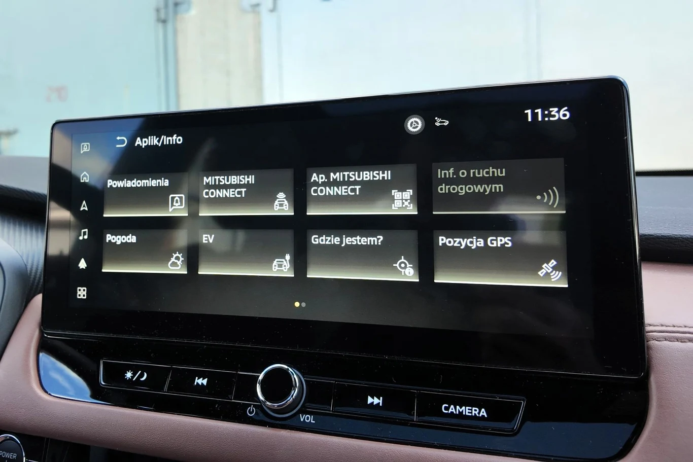 Ekran systemu multimedialnego samochodu z wyświetlonym menu głównym zawierającym ikony aplikacji takich jak powiadomienia, MITSUBISHI CONNECT, informacje o ruchu drogowym, pogoda, EV, lokalizacja GPS oraz godzina w prawym górnym rogu.