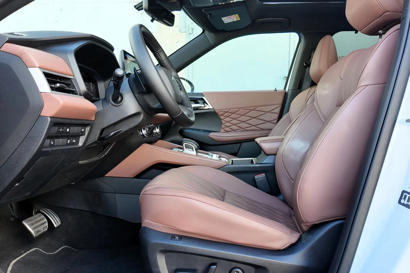 Luksusowe wnętrze samochodu z brązową, skórzaną tapicerką, przestronnym fotelem kierowcy i pasażera, wielofunkcyjną kierownicą oraz nowoczesnym panelem sterowania przy konsoli centralnej.