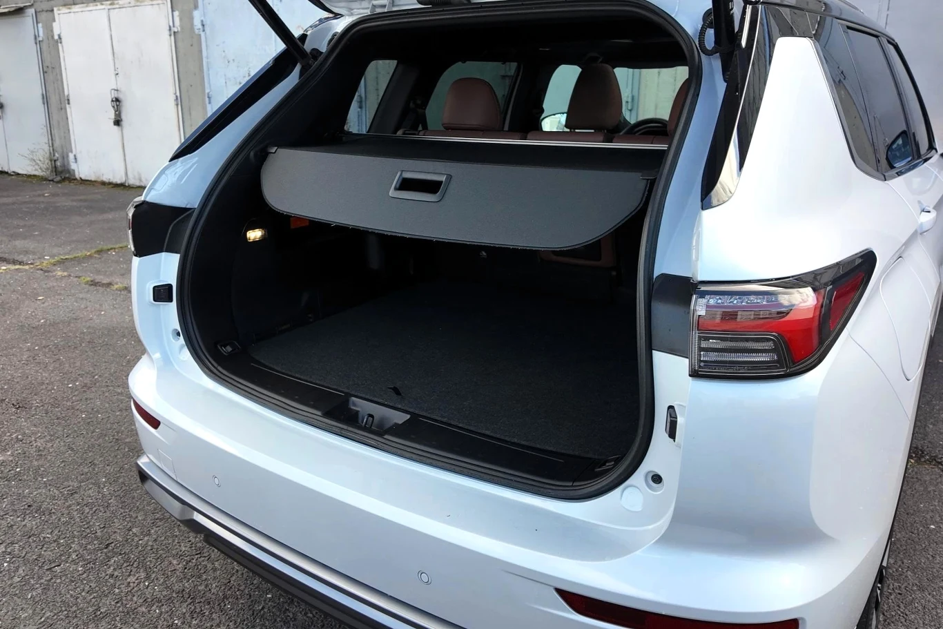 Otwarty bagażnik białego SUV-a z rozłożoną roletą zasłaniającą zawartość przestrzeni bagażowej, tylne siedzenia widoczne w tle.