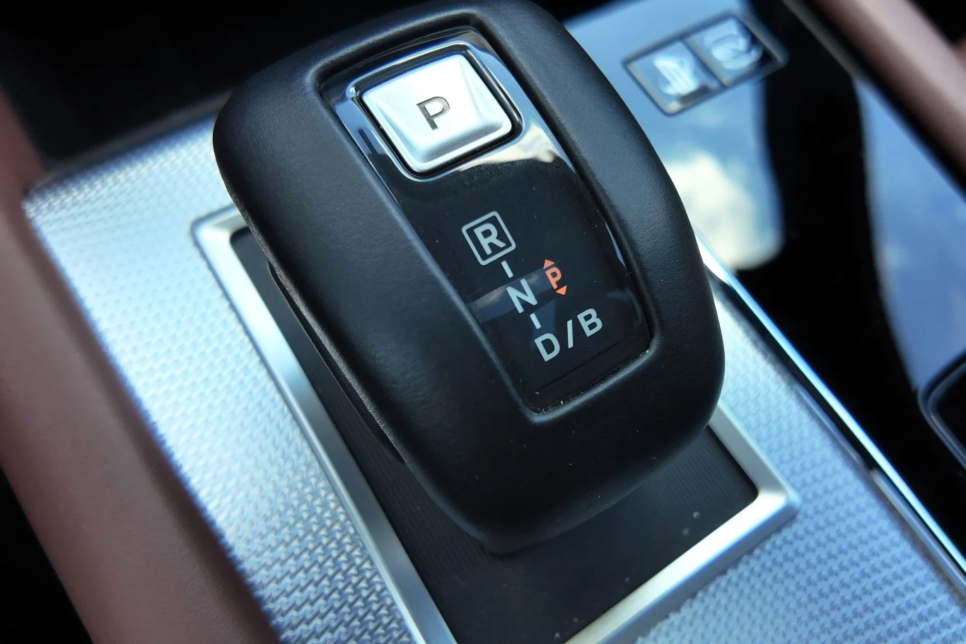 Czarny selektor automatycznej skrzyni biegów z wyraźnie oznaczonymi trybami P, R, N, D/B, umieszczony na srebrnej, metalizowanej konsoli centralnej samochodu.