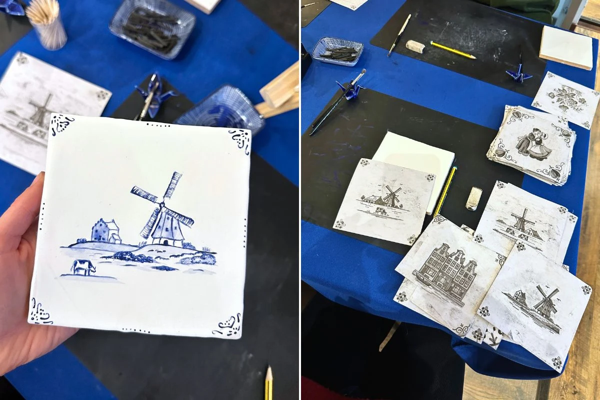 Ręcznie malowane kafelki z motywami krajobrazów, w tym wiatraków i zamków, ułożone na stole z niebieskimi narzędziami do malowania, pędzlami i kartkami pomocniczymi.