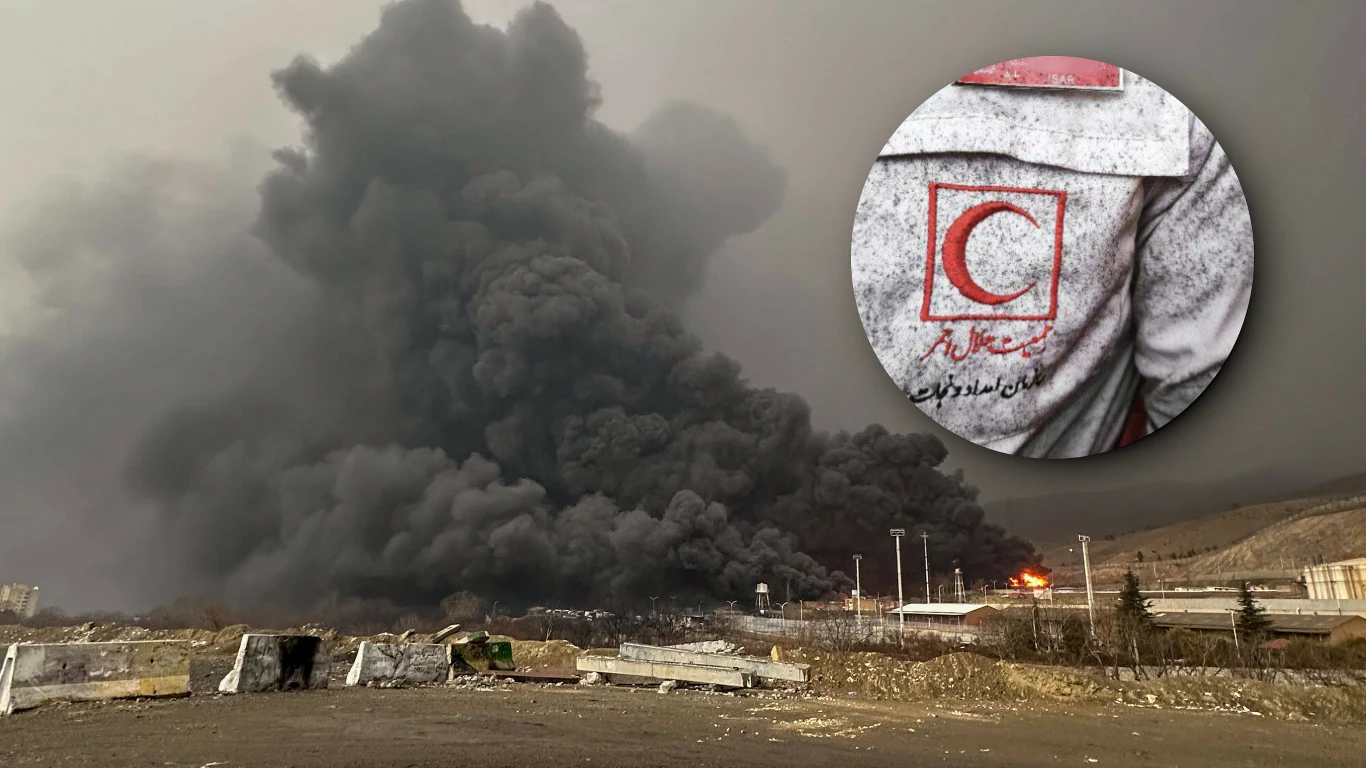 Gęste kłęby czarnego dymu unoszące się nad terenem przemysłowym w wyniku pożaru, w prawym górnym rogu zbliżenie na logo Czerwonego Półksiężyca na tle zabrudzonego ubrania ratownika.