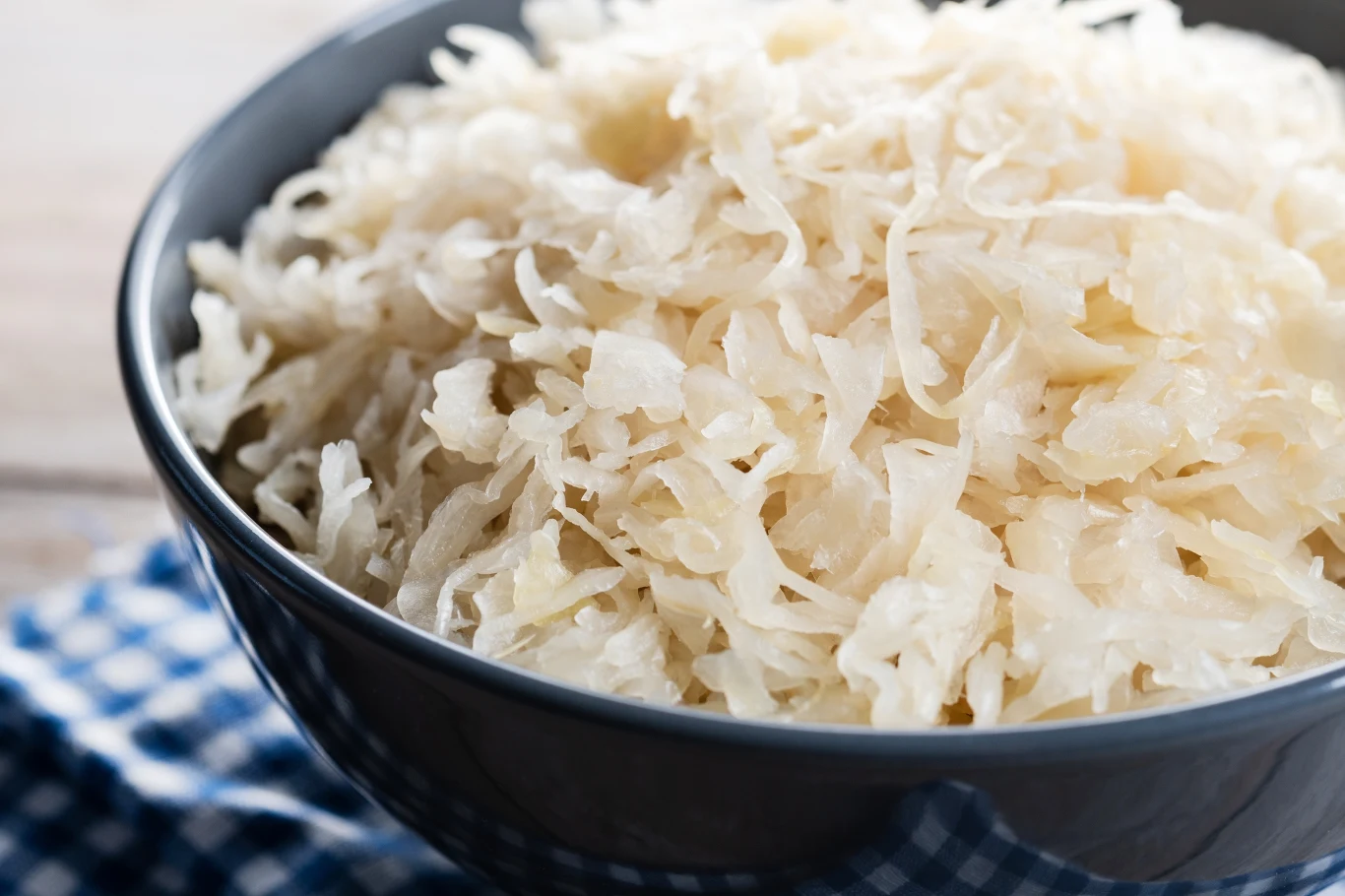 Miska wypełniona świeżą, białą kiszoną kapustą, ustawiona na niebiesko-białej kraciastej serwetce.