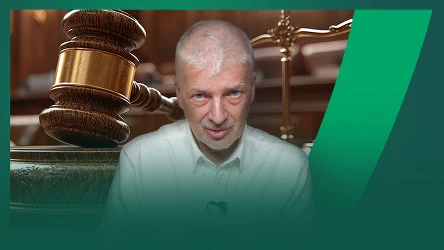 Starszy mężczyzna w białej koszuli na tle dużego drewnianego młotka sędziowskiego i wnętrza sali sądowej.