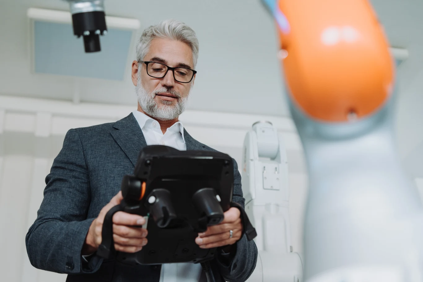 Średni wiek założyciela najszybciej rosnących startupów to 45 lat, a prawdopodobieństwo sukcesu rośnie z wiekiem aż do ok. 55–60 lat Mężczyzna w garniturze obsługuje panel sterujący do ramienia robota w laboratorium technologicznym.