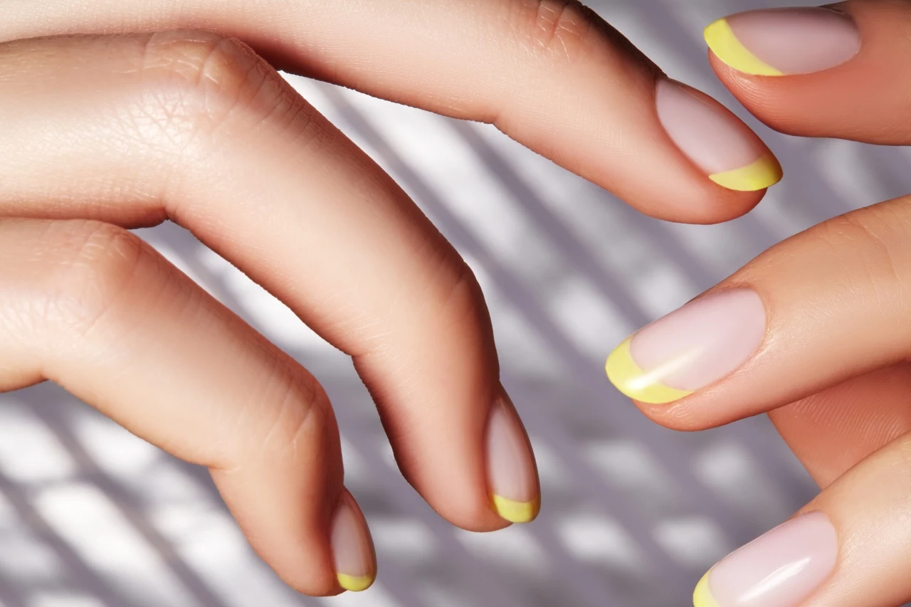 Dłonie z zadbanymi paznokciami ozdobionymi pastelowym, żółtym frenchem na naturalnej płytce paznokcia.