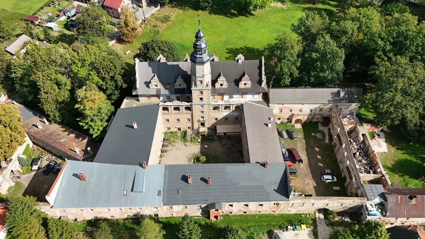Pałac w Gorzanowie w Kotlinie Kłodzkiej. Obiekt z wieżą i zabudowaniami gospodarczymi, otoczony zielenią. Widok z lotu ptaka.