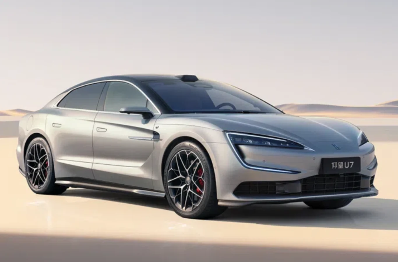 Sedan Yangwang U7. Srebrny, nowoczesny sedan elektryczny o dynamicznej sylwetce, masywnych felgach z czarnymi akcentami oraz wąskich, futurystycznych reflektorach LED, ustawiony na jasnym tle pustynnym.