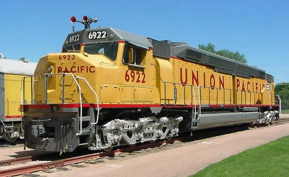 Żółto-szara lokomotywa Union Pacific o numerze 6922 stoi na torach, wyróżnia się dużymi, czerwonymi literami na boku oraz charakterystycznym, masywnym przodem z rzucającym się w oczy numerem umieszczonym nad szybą maszynisty.