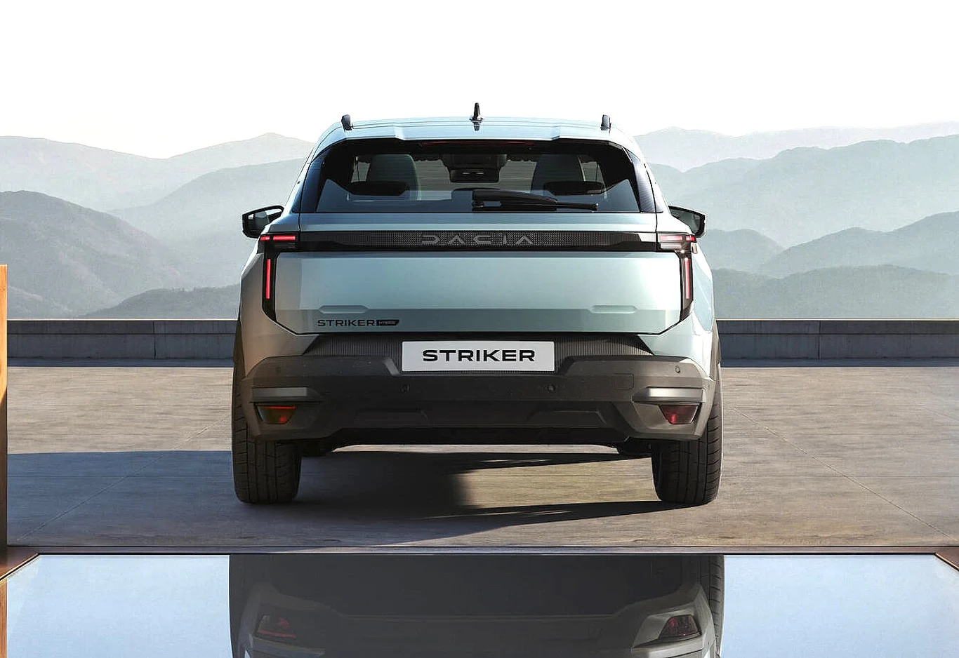 Nowoczesny samochód Dacia Striker widoczny od tyłu, z charakterystycznym szerokim pasem świetlnym, wyrazistymi liniami i oznaczeniem modelu, ustawiony na tle górskich krajobrazów.