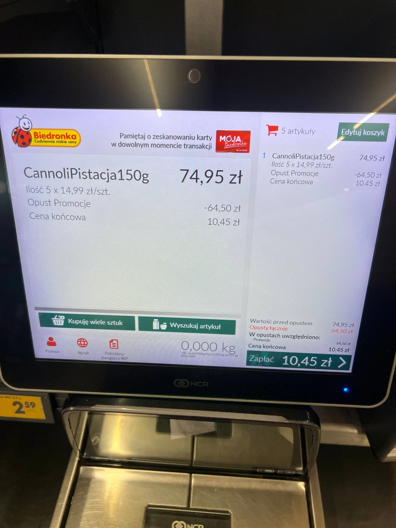 Ekran kasy samoobsługowej w sklepie Biedronka wyświetla produkt Cannoli Pistacja 150g, pierwotną cenę 74,95 zł, informację o promocji obniżającej cenę o 64,50 zł oraz cenę końcową 10,45 zł, z wyraźnie widocznym podsumowaniem zakupu po prawej stronie ek...