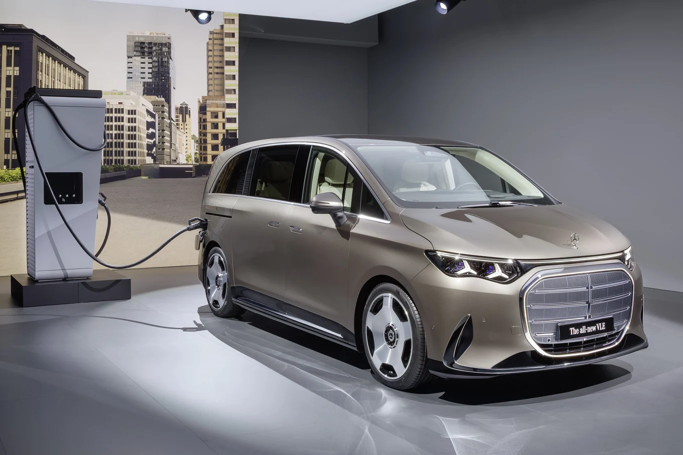 Nowoczesny samochód elektryczny klasy premium w kolorze szarym podłączony do stacji ładowania w minimalistycznym, dobrze oświetlonym pomieszczeniu, z tłem przedstawiającym panoramę miejską.