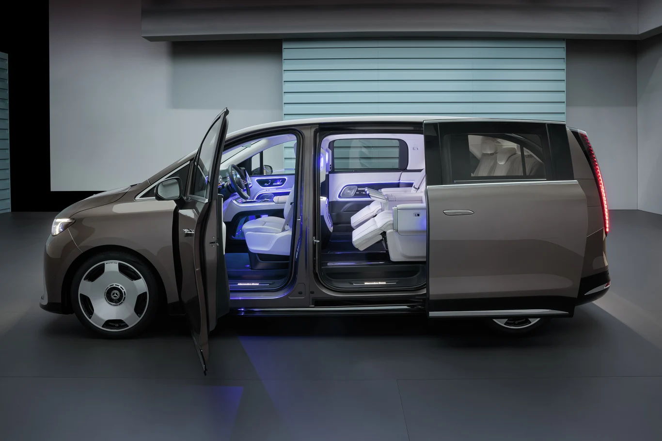Nowoczesny minivan w metalicznym kolorze z otwartymi drzwiami bocznymi, eksponujący przestronne i luksusowe wnętrze z białymi skórzanymi fotelami oraz ambientowym oświetleniem LED.