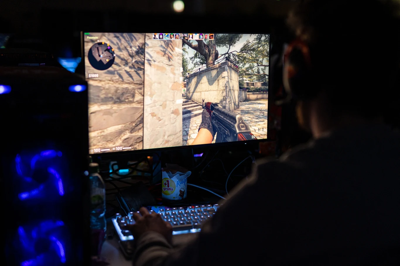 Osoba gra w Counter-Strike na komputerze, używając klawiatury i myszki, ekran pokazuje interfejs gry z celownikiem.