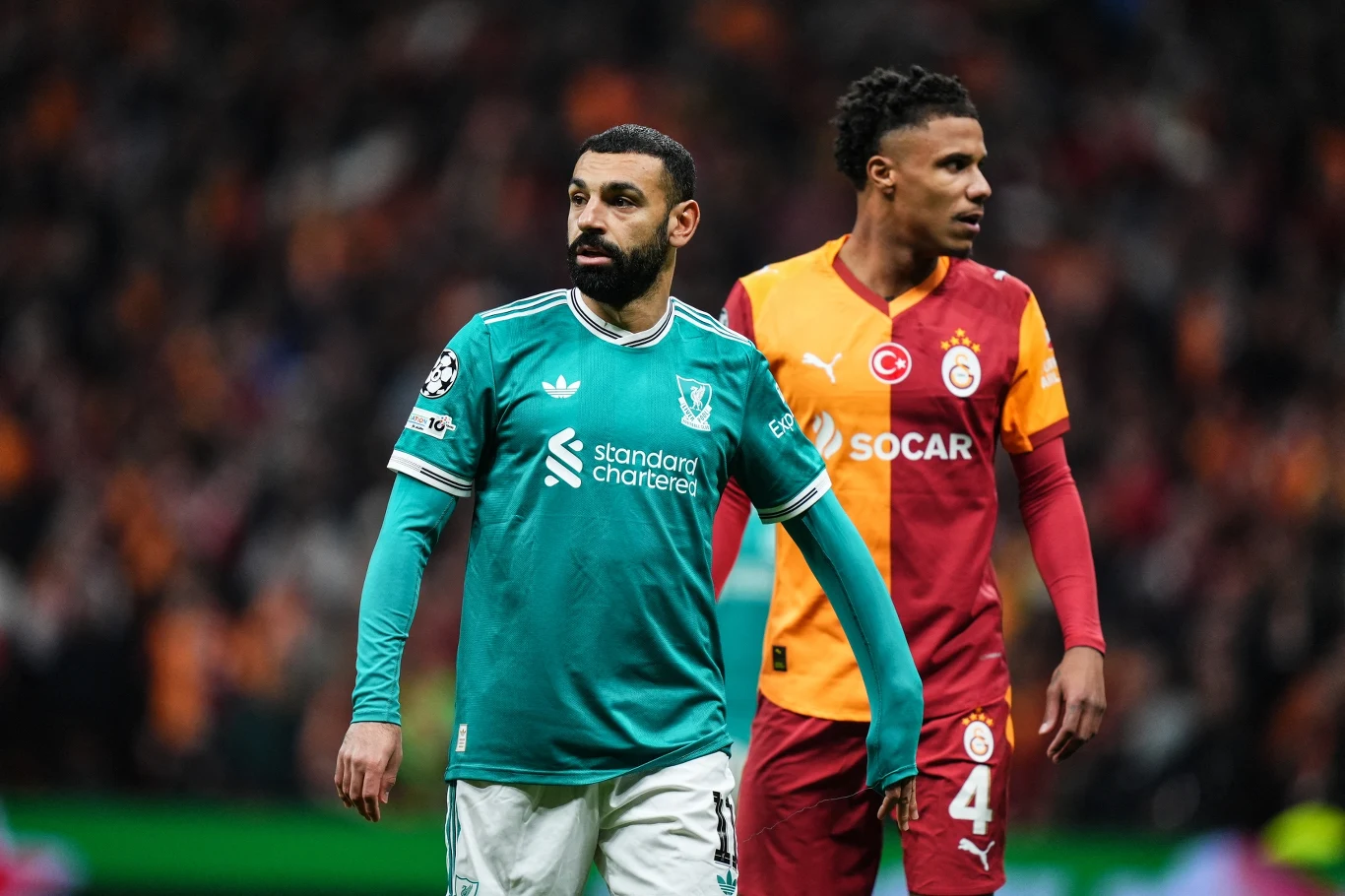 Dwóch piłkarzy podczas meczu – zawodnik w zielonym stroju Liverpoolu z przodu oraz gracz Galatasaray w żółto-czerwonym stroju w tle, obaj skupieni na boiskowych wydarzeniach.