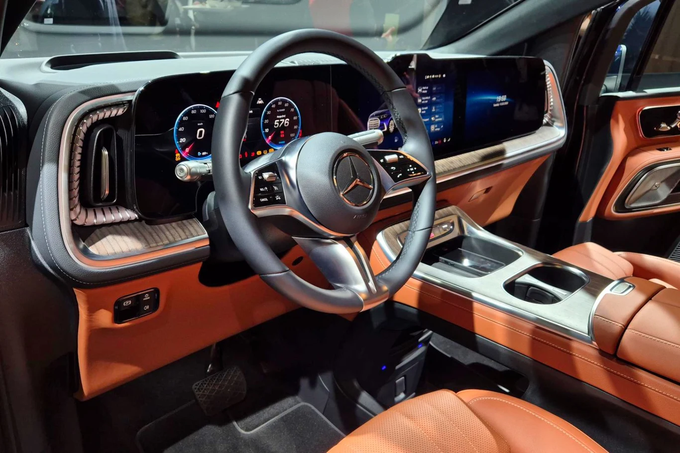 Luksusowe wnętrze samochodu Mercedes z dużymi, cyfrowymi wyświetlaczami na desce rozdzielczej, sportową kierownicą oraz skórzanymi, pomarańczowymi fotelami i wykończeniem, podkreślające nowoczesny charakter i wysoki standard wyposażenia.