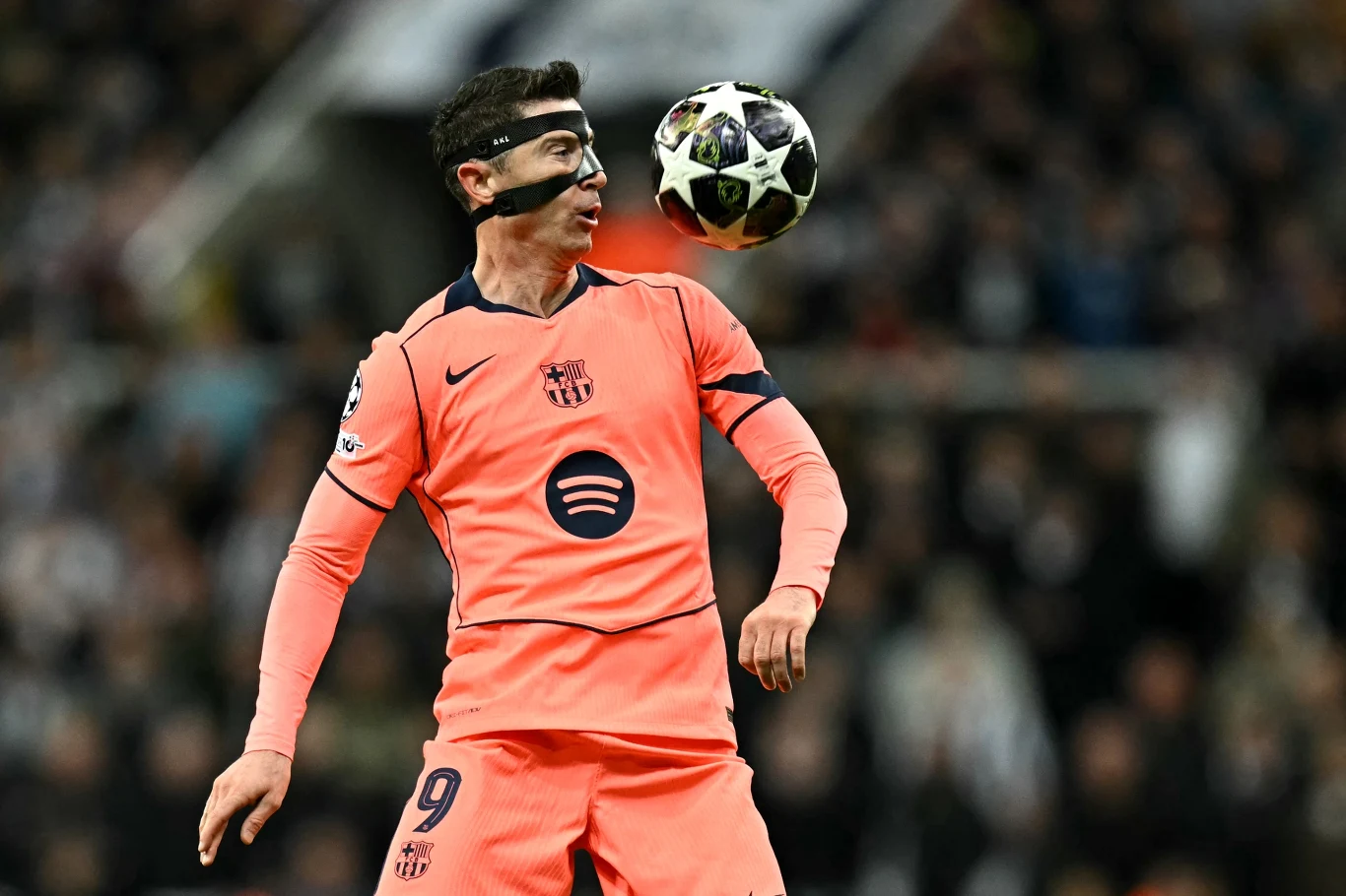 Piłkarz Barcelony ubrany w różowy strój i czarną maskę kontroluje lecącą piłkę nożną podczas meczu na stadionie, skoncentrowany na grze, w dynamicznej pozie.