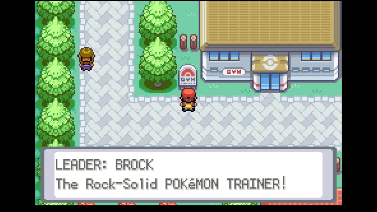 Trener Pokémon stoi przed wejściem do budynku sali gimnastycznej z tablicą informacyjną, na której widnieją informacje o liderze Brocku i jego przydomku, otoczony ścieżkami, drzewami oraz innym przechodniem.